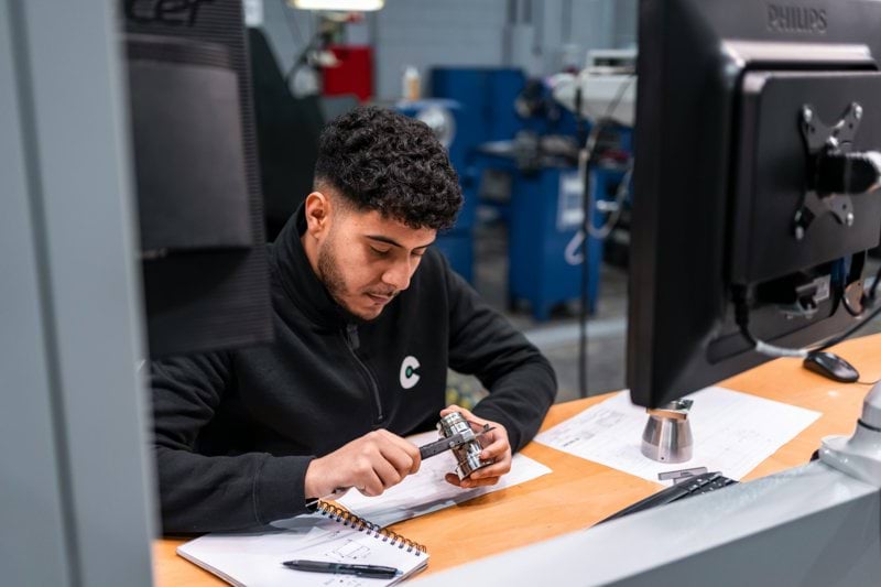 A man measures a metal component carefully.
