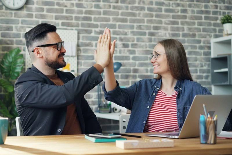 a man and a woman sitting at a table high fiving each other