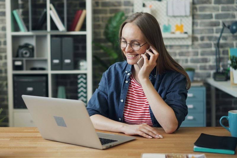 a woman talking on a cell phone while using a laptop
