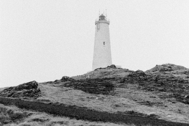 A lighthouse stands on a grassy hill.
