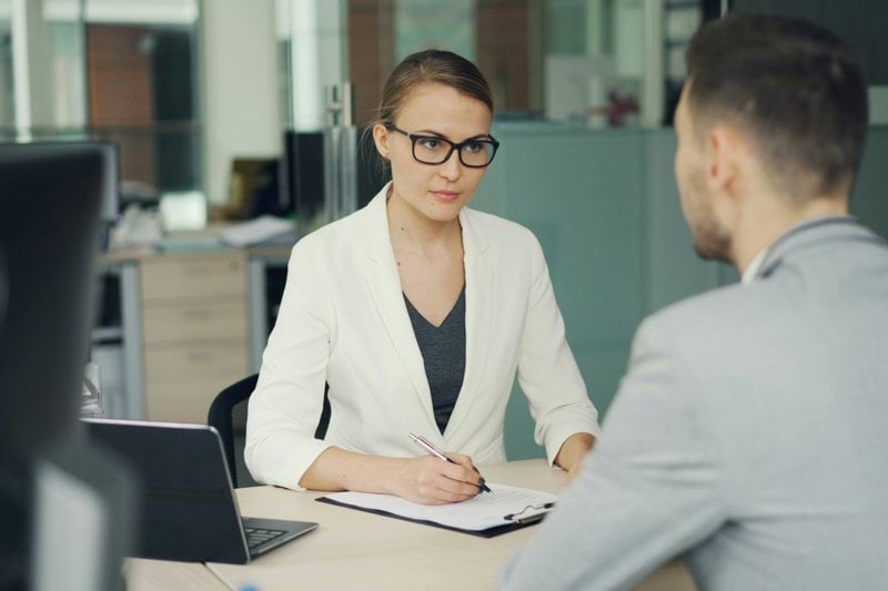 Woman in glasses interviews man at office desk