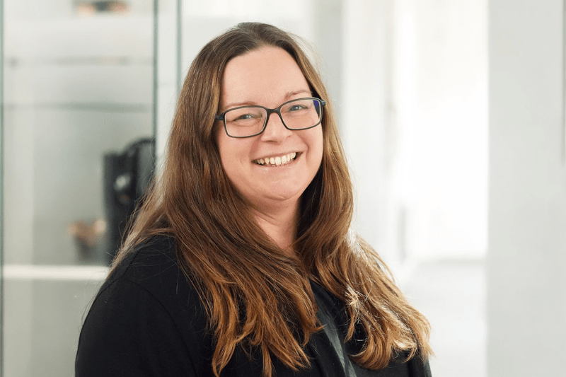 Kvinna med långt hår och glasögon ler in i kameran