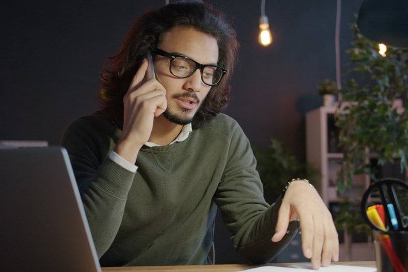 Man talking on phone at desk with laptop