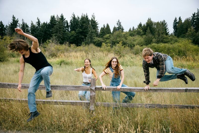 Four friends climbing over a wooden fence outdoors