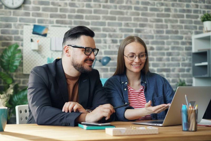 a man and a woman sitting at a table looking at a laptop