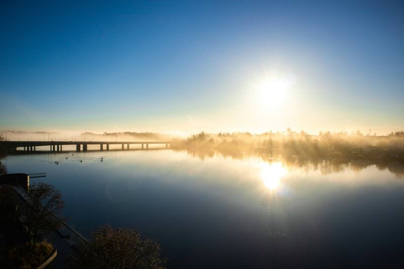 the sun is setting over a lake with a bridge in the background