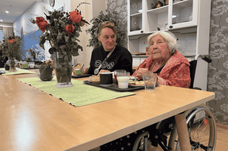 Kaskiniityn johtaja Katri asukkaan kanssa yhdessä lounaspöydässä, pöydällä kukkia