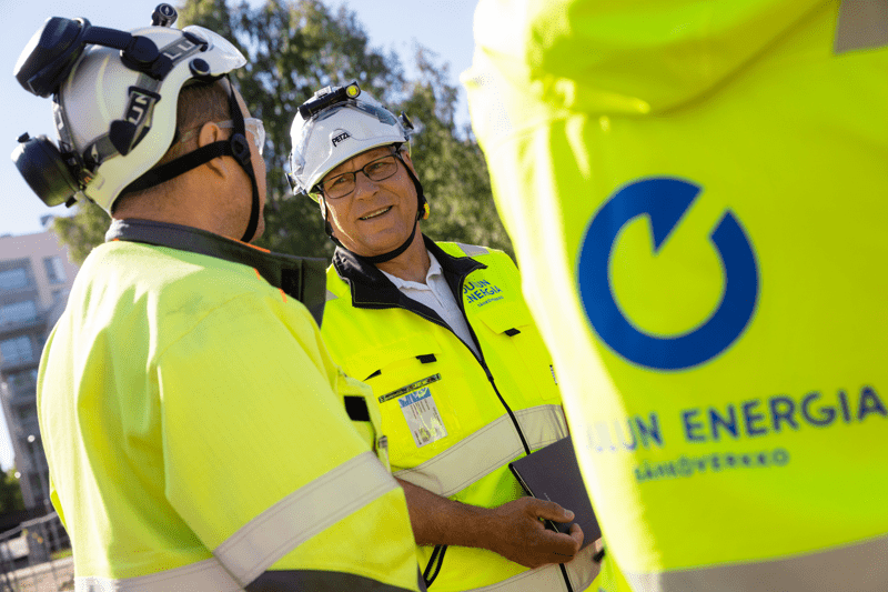 Sähköverkkojen työntekijät juttelevat iloisesti toisilleen työmaalla. 