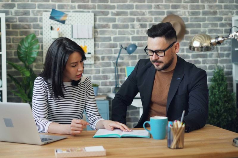 a man and a woman sitting at a table looking at a laptop