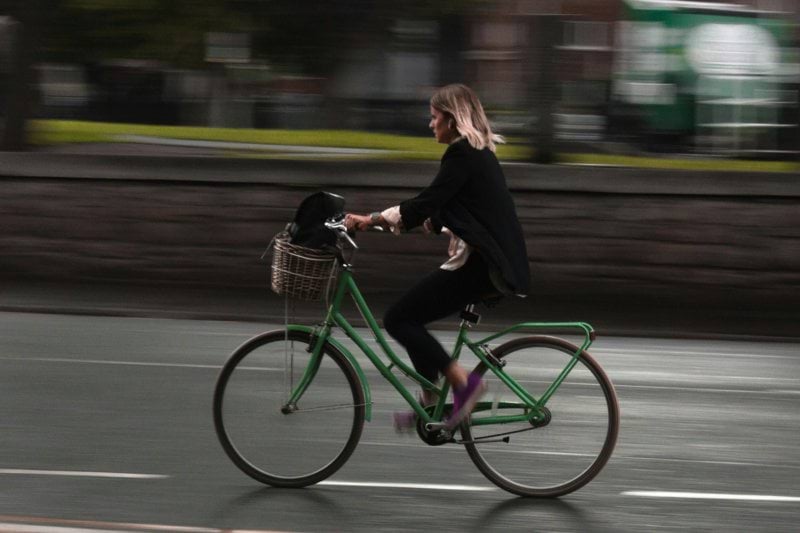 woman riding green commuter bike with brown basket