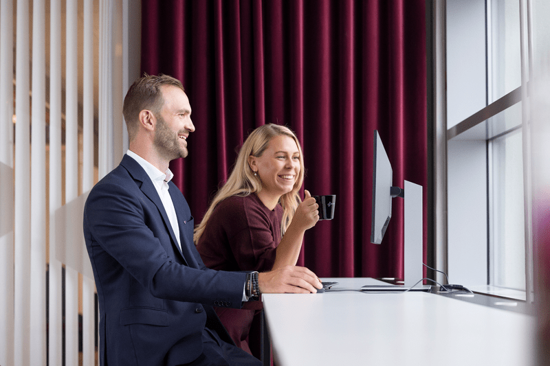 Två kollegor samtalar vid skrivbord i kontor.