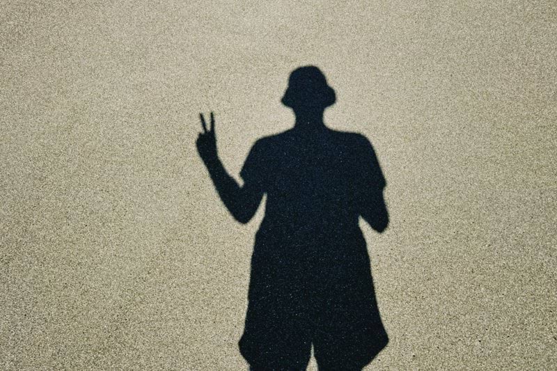 Shadow of a person wearing a hat making peace sign