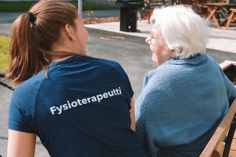 Attendon fysioterapeutti ikäihmisen kanssa hoivakodin pihalla