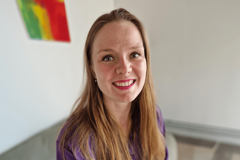 Närbild i liggande format på Johanna i utsläppt hår. Vit bakgrund med tavla i starka färger