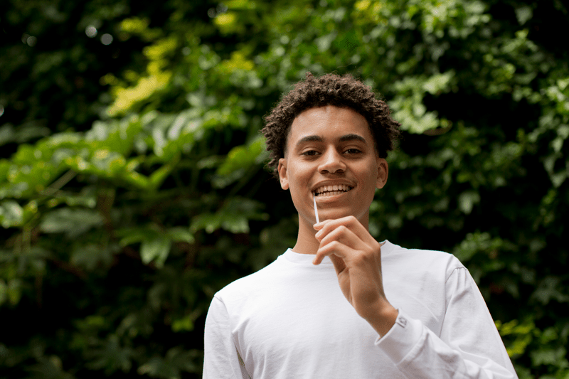 Young man signing up to the stem cell register, looking at the camera whilst swabbing inside his cheek