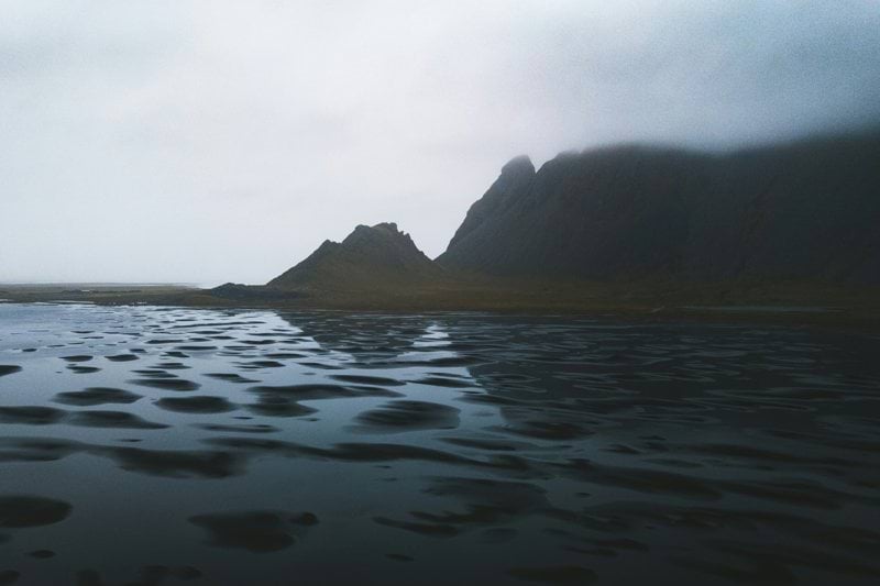 Mountains reflect in a dark, wet landscape.