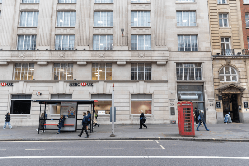 Street view of a large stone building with an HSBC bank, a bus stop, and a red telephone box