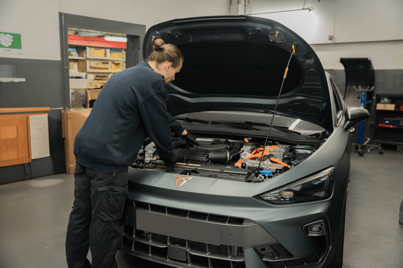 Mécanicien en tenue professionnelle, ouvrant le capot d'une voiture pour inspecter les mécanismes, montrant une attention aux détails et au diagnostic.