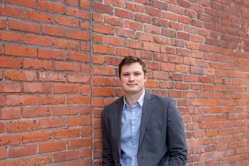 man in black suit jacket standing beside brown brick wall