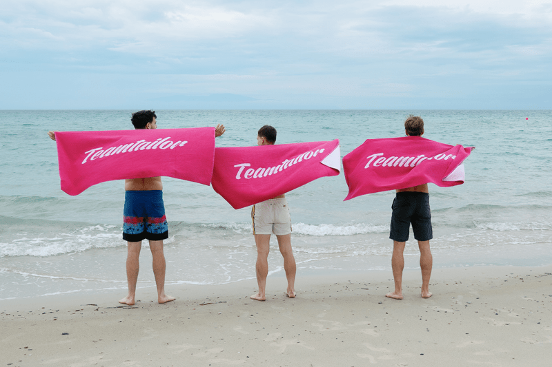 Three people on beach holding Teamtailor towels