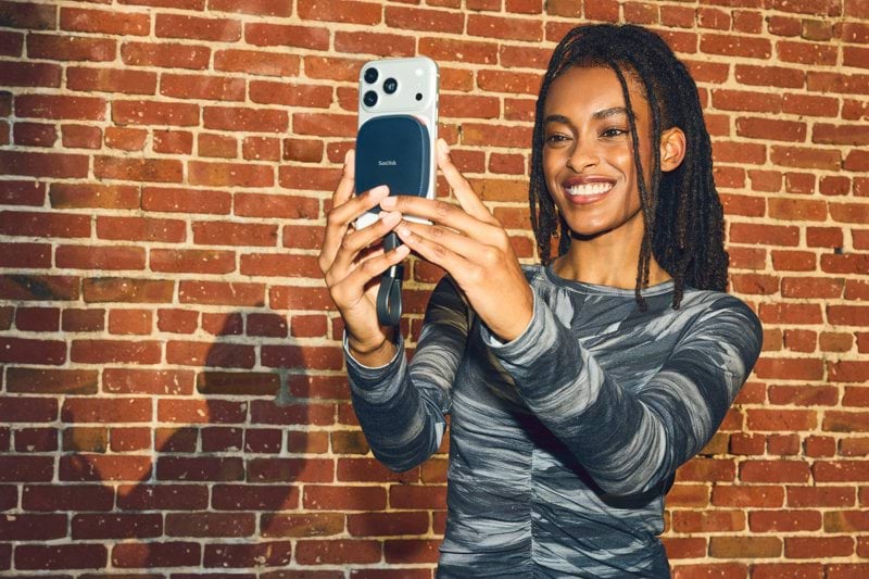 Smiling woman takes a selfie with smartphone against brick wall