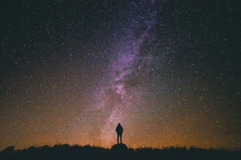 silhouette of man standing on rock while looking in sky