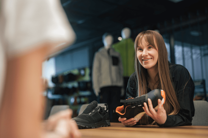 Woman holding a shoe, smiling and looking at a colleague