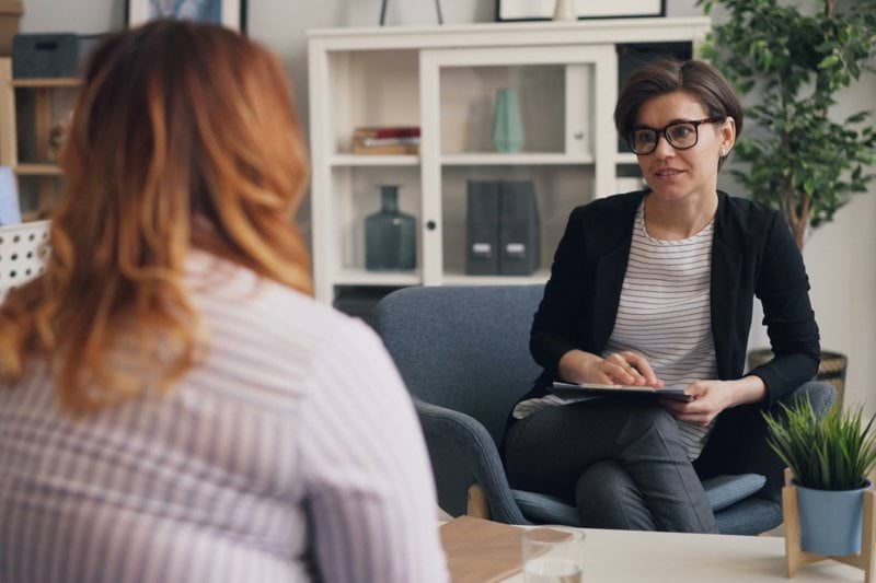 a woman sitting in a chair talking to another woman