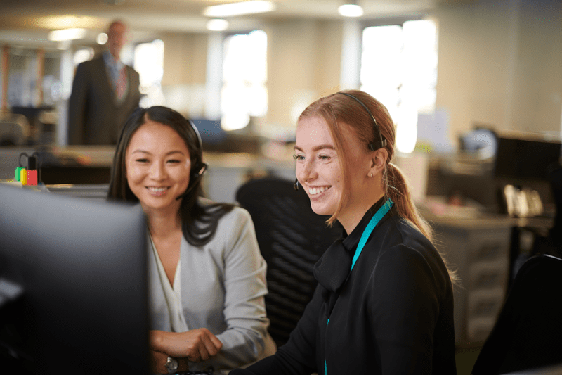 Two women sitting in an office, looking at a computer screen and smiling