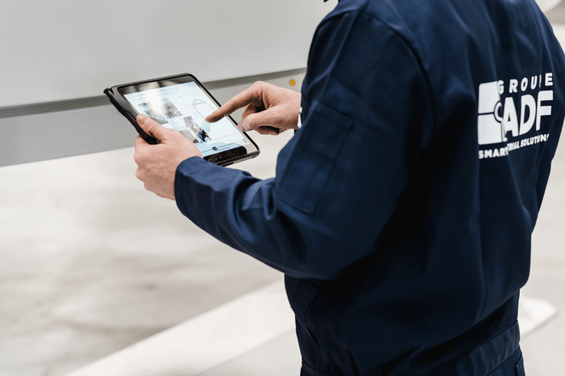 Gros plan de profil d'un collaborateur du Groupe ADF en veste de travail bleu marine, utilisant une tablette tactile dans un atelier industriel.