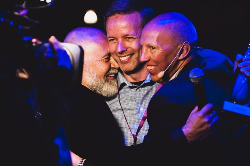 Medarbetare firar eller omfamnar varandra under scenaktivitet på företagsevent.