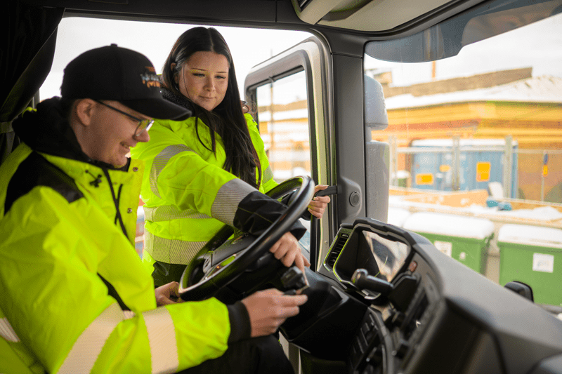 Två arbetare i varselkläder inne i en lastbilshytt.