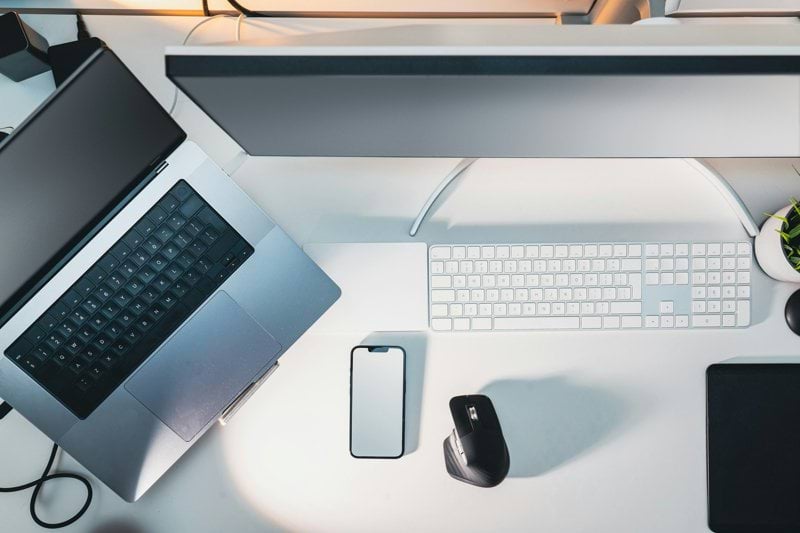 a desk with a laptop, keyboard, mouse and a cell phone
