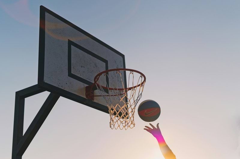 A vibrant hand shoots a basketball towards an outdoor hoop
