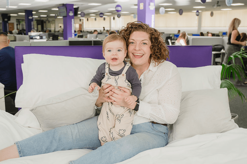 Mother and baby smiling, sat on a bed