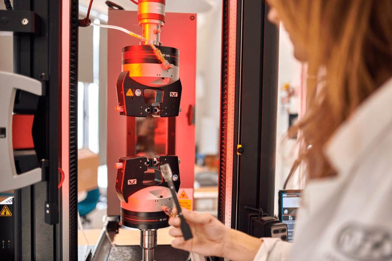 A scientist stands in front of a complex laboratory machine that emits a bright red light.
