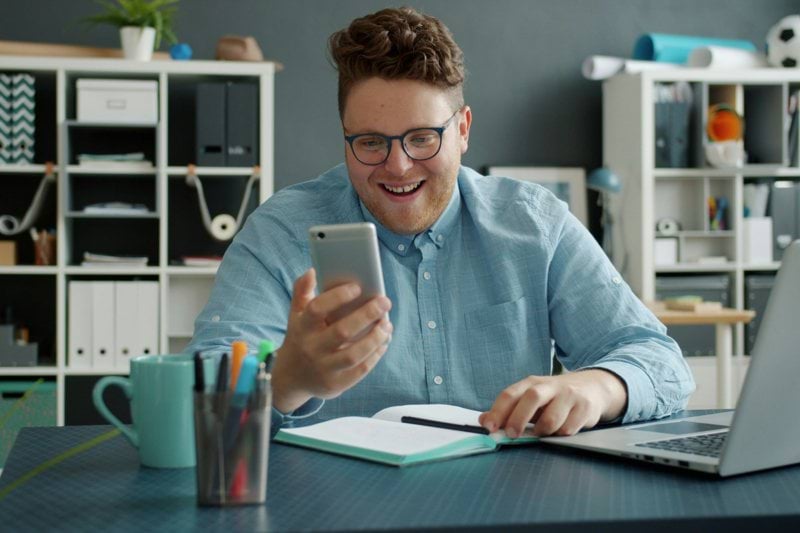 Man smiling while looking at his phone at desk