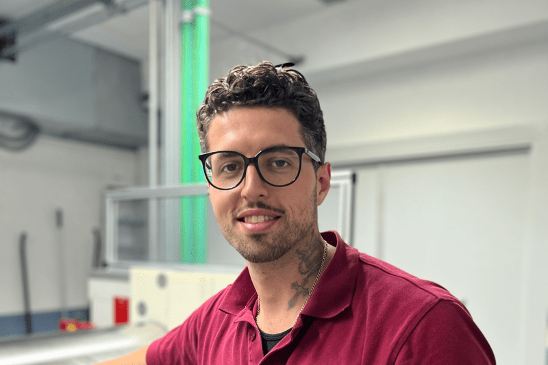Ein Mann in der Produktion arbeitet an einer Maschine und schaut in die Kamera.