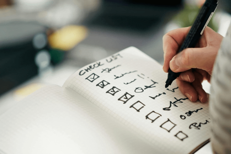Hand mit Stift schreibt eine Checkliste in ein Notebook