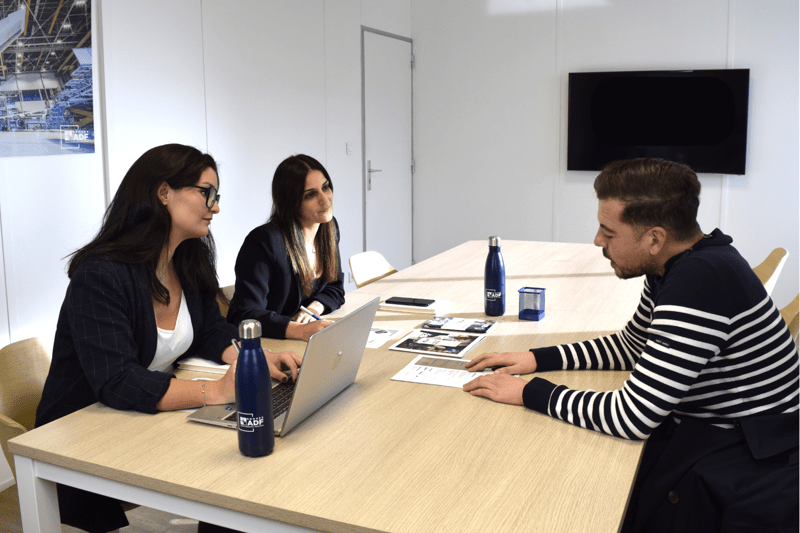 Una responsable operativa y una reclutadora realizan una entrevista de trabajo con un candidato sentado frente a ellas alrededor de una mesa de reuniones.