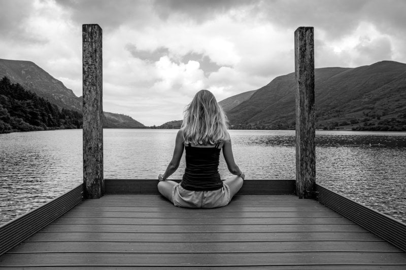 A woman sitting on a dock in front of a body of water