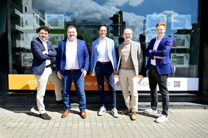Five smiling men posing in front of a building
