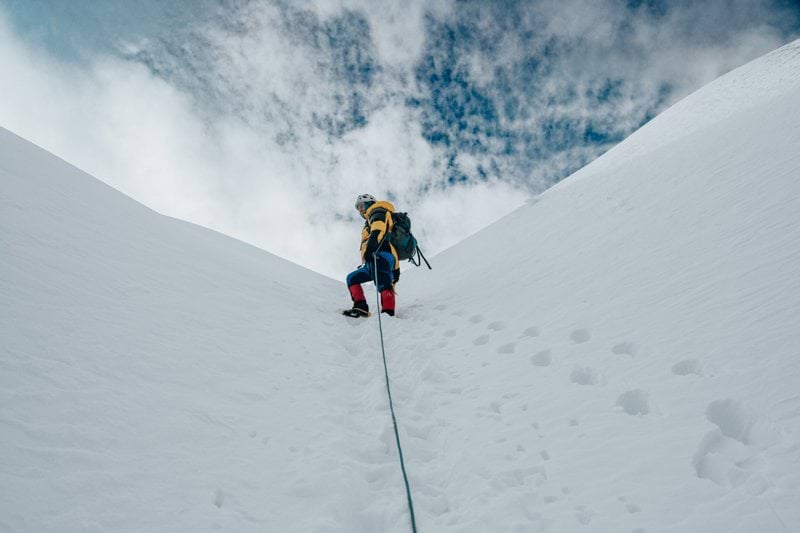 A climber ascends a snowy mountain, reaching for the sky.