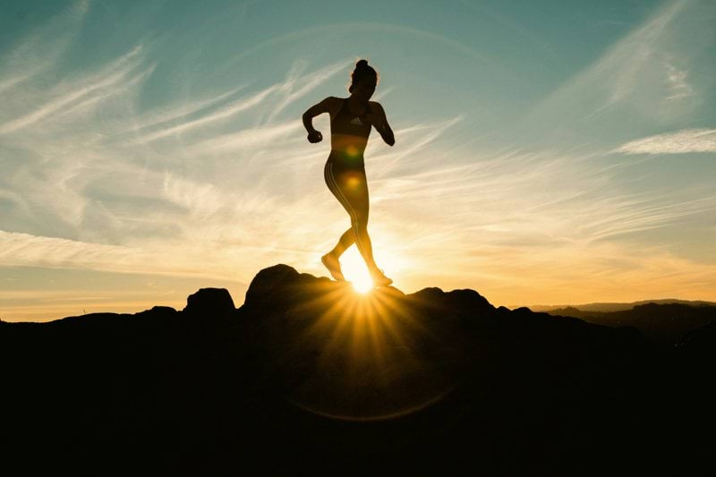 a silhouette of a woman running on a hill at sunset