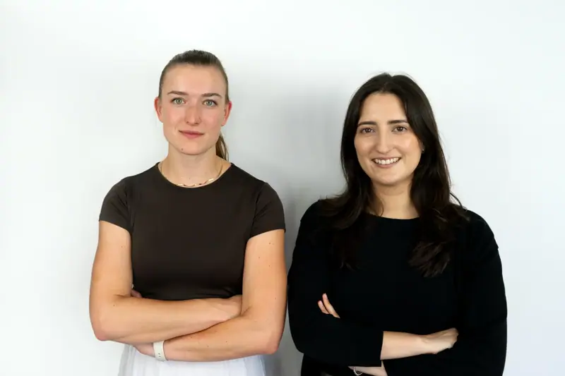 Two colleagues standing side by side against a light background, smiling at the camera.