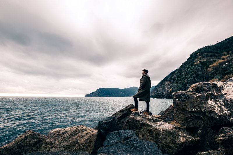 man standing on boulder near body of water