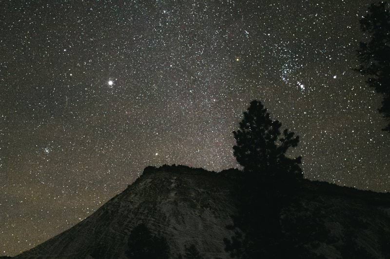 Starry night sky over a silhouetted mountain peak.