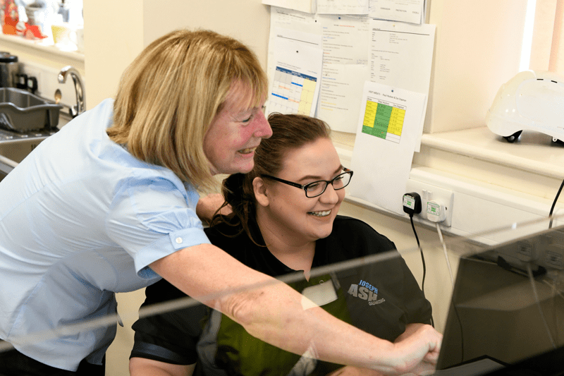 two office workers pointing at computer smiling