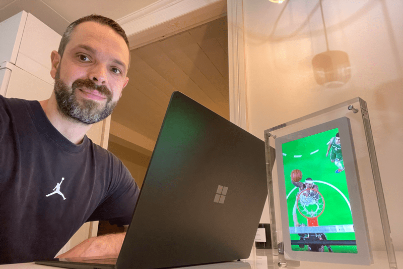 Porträtt av en medarbetare på Advania, Rade, leende framför datorn i sitt hemmakontor vid köksbordet.