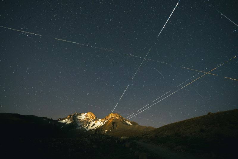 Long exposure light trails crossing a starry night sky above a snow-capped mountain